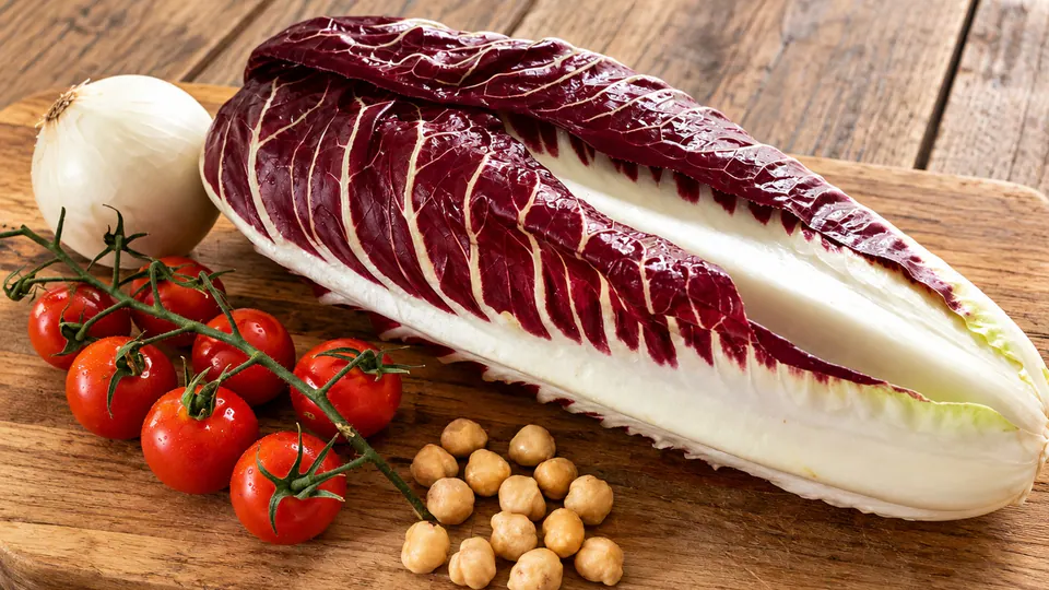 Un cespo di Radicchio Precoce su un tagliere, con pomodorini, cipolla e ceci